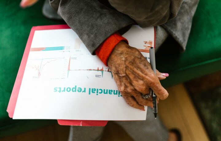 Close-up of an elderly woman holding a pen with a financial report.