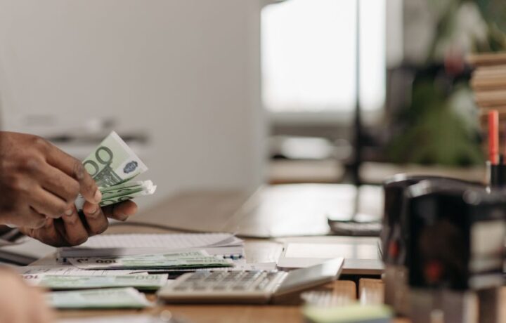Close-up of hands counting euro bills at an office desk with a calculator.