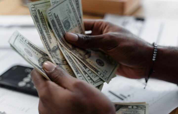 Detailed image of hands counting US dollar bills on a desk, emphasizing finance and budgeting.