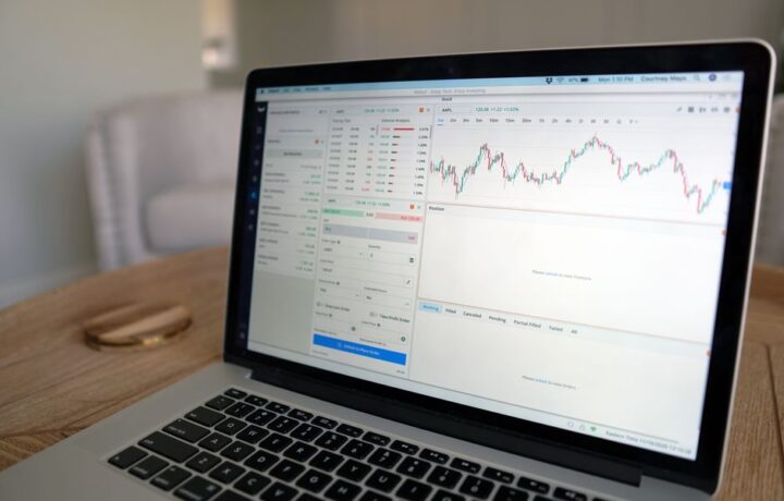 Close-up of a laptop displaying stock trading software with a market chart on a wooden table.