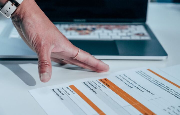 Close-up of a hand reviewing a financial report on a laptop, indicating focus on business analysis.