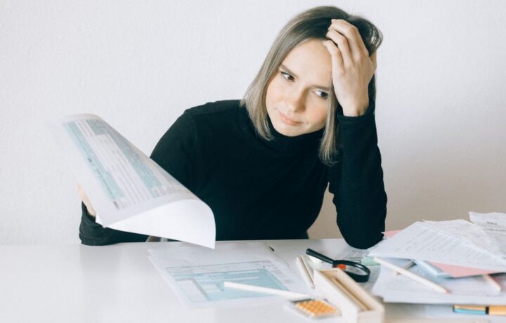 A woman showing stress while reviewing multiple paperwork and financial documents at a desk.