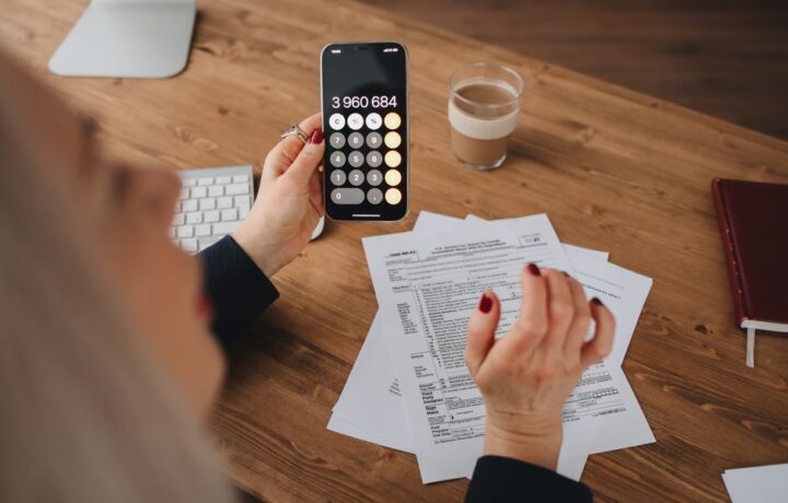 A woman calculates on her smartphone while working with documents at a desk.