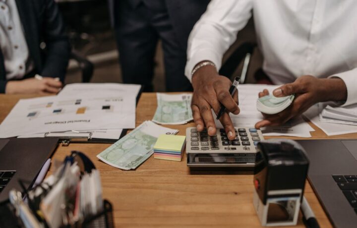 Professional setting with people handling cash and calculations using a calculator at a desk.