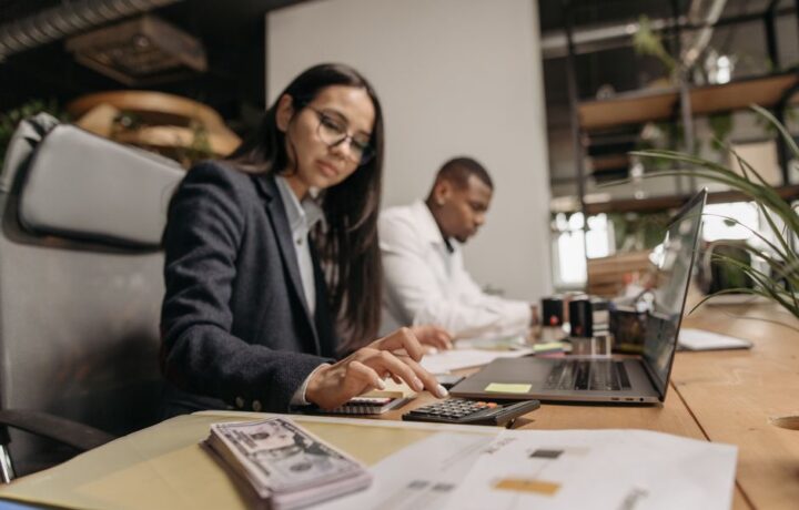 Two business professionals collaborating with a laptop and calculator in a modern office.