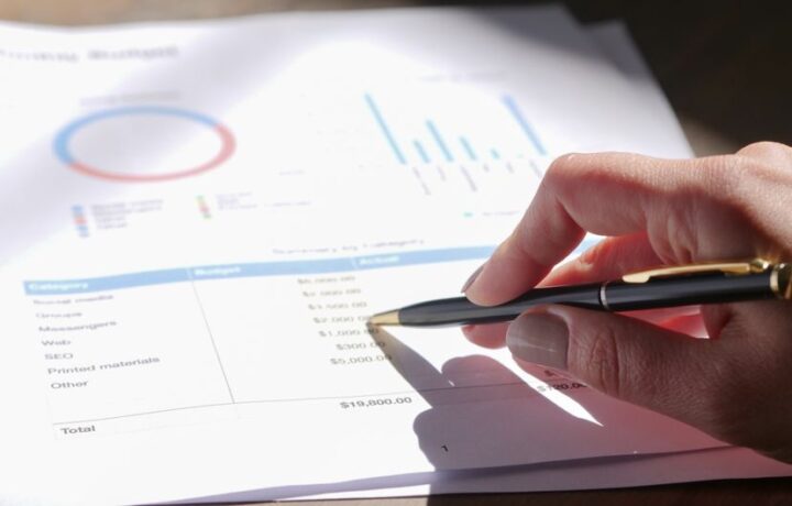 Hand holding pen, analyzing budget with charts and graph paper.