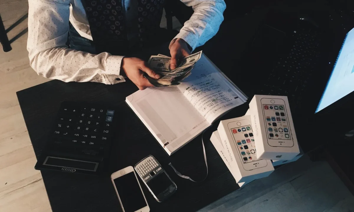 Profissional organizando finanças com dispositivos tecnológicos e dinheiro em uma mesa, ilustrando gestão de caixa