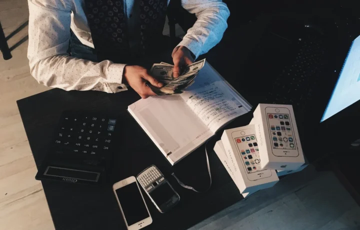 Profissional organizando finanças com dispositivos tecnológicos e dinheiro em uma mesa, ilustrando gestão de caixa