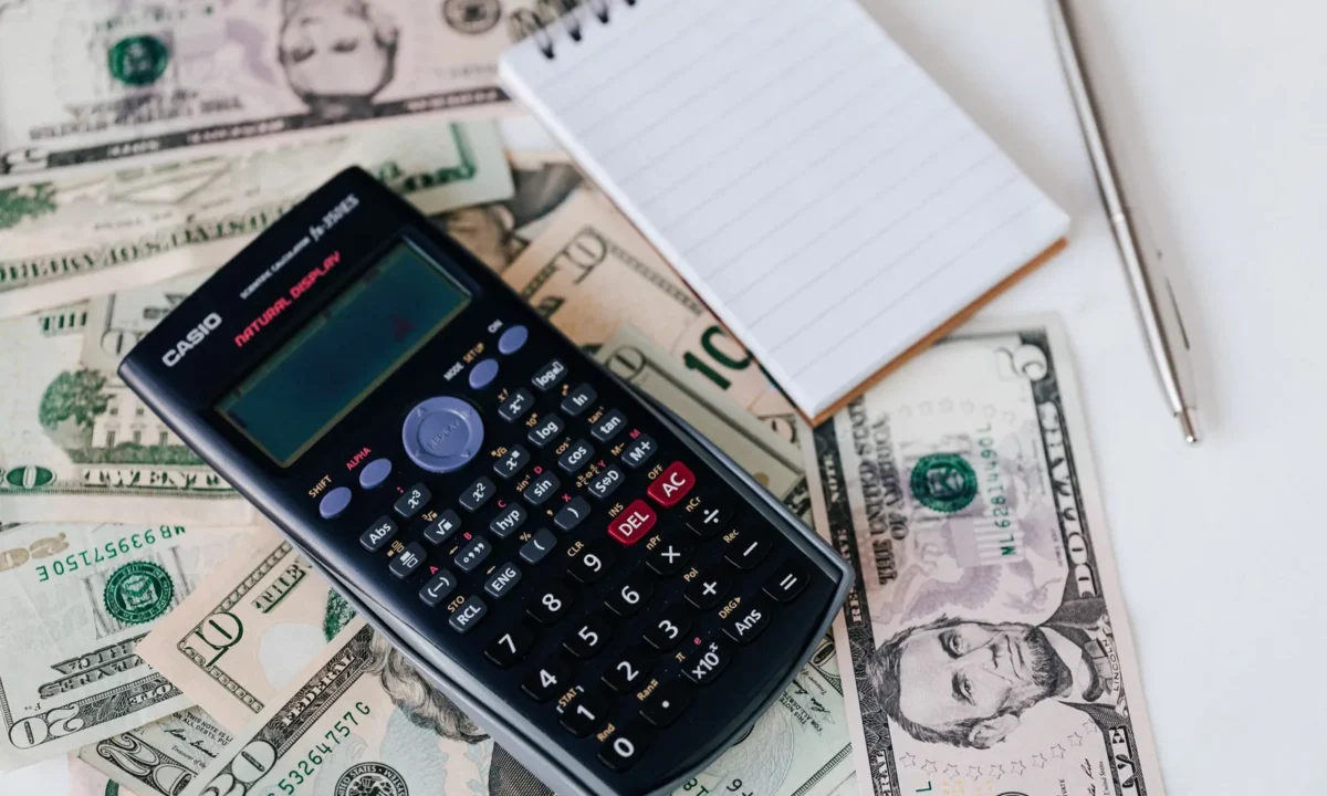 Calculadora eletrônica e caderno sobre notas de dólar, representando planejamento financeiro e como fazer fluxo de caixa