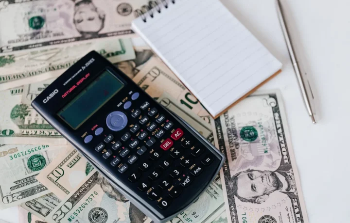 Calculadora eletrônica e caderno sobre notas de dólar, representando planejamento financeiro e como fazer fluxo de caixa