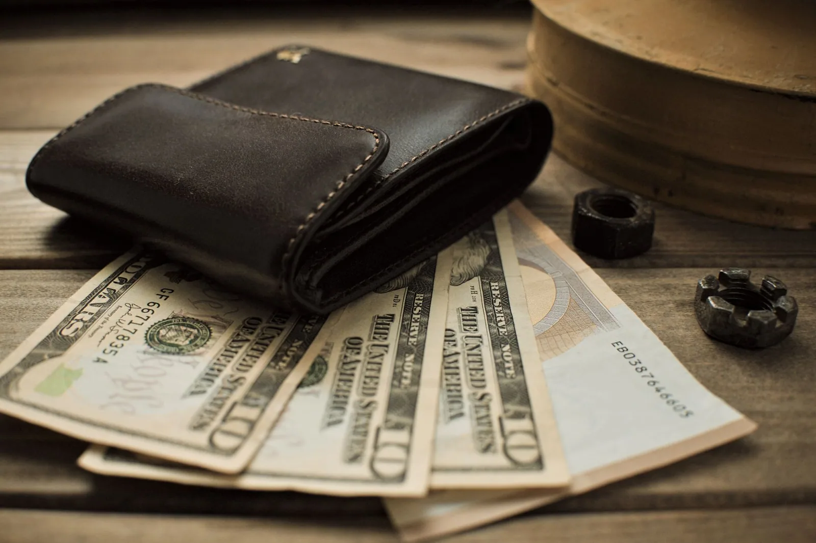 Detalhe de uma carteira de couro com notas de dólar em uma mesa de madeira, ilustrando a separação de contas financeiras