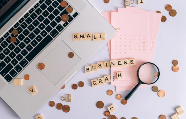 Disposição de laptop, moedas e letras de scrabble formando 'crash de pequenos negócios' em um ambiente de trabalho