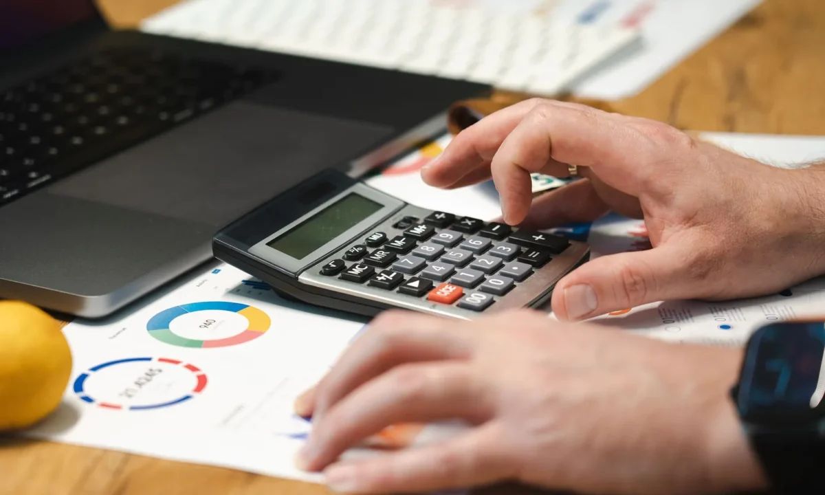 Empreendedor comparando o melhor sistema financeiro para MEI no notebook com calculadora na mesa