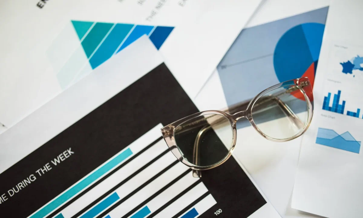 Óculos sobre documentos financeiros com gráficos, simbolizando a antecipação de receitas e planejamento financeiro