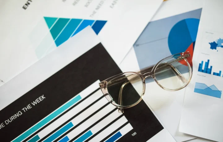 Óculos sobre documentos financeiros com gráficos, simbolizando a antecipação de receitas e planejamento financeiro