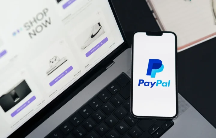 Smartphone com logo do PayPal ao lado de um laptop com site de compras, representando aplicativos de controle financeiro