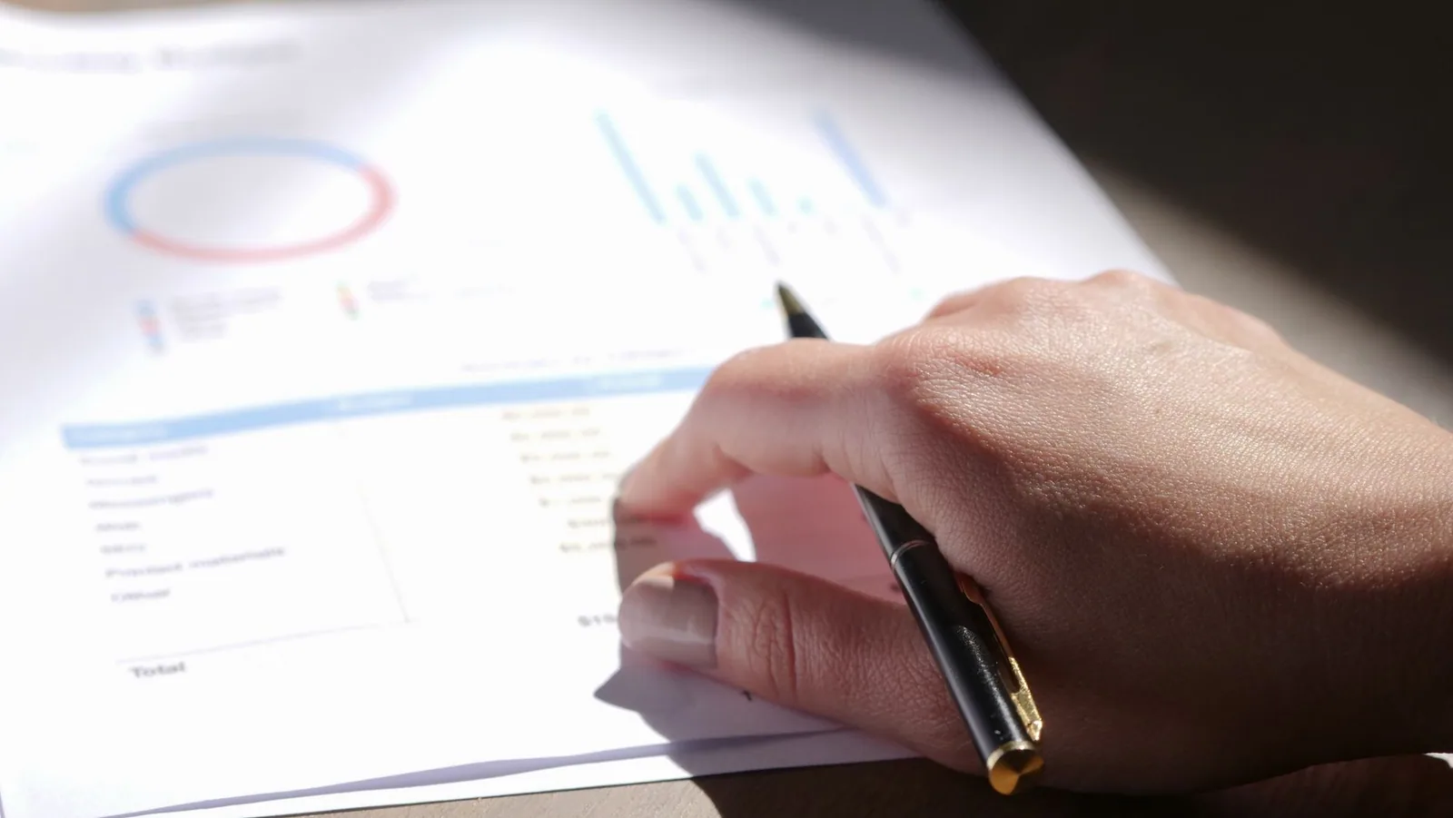 Mão com caneta analisando gráficos financeiros impressos em papel